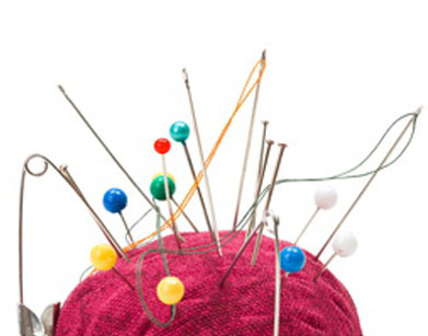 Push pins, needles and safety pins clustered in pincushion