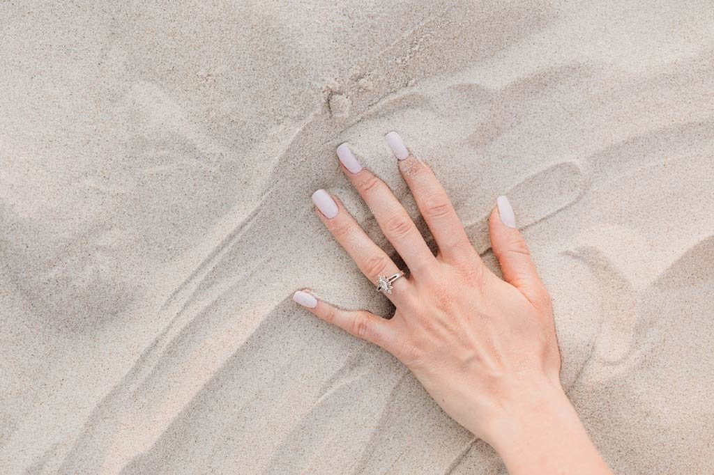 Mano de mujer con uñas pintadas sobre la arena