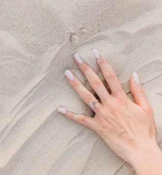 Mano de mujer con uñas pintadas sobre la arena